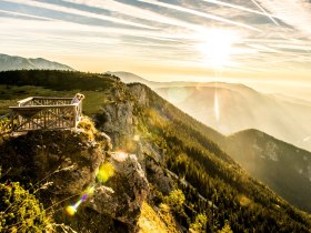 Die goldenen Strahlen der Sonne brechen durch die Wolken und tauchen die majestätischen Berge in ein warmes Licht. Ein atemberaubender Ausblick auf die sanften Hügel und dichten Wälder lädt dazu ein, die frische Bergluft zu genießen und die Seele baumeln zu lassen.