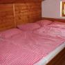 Three beds with red and white checked comforter covers in a wood-paneled room.