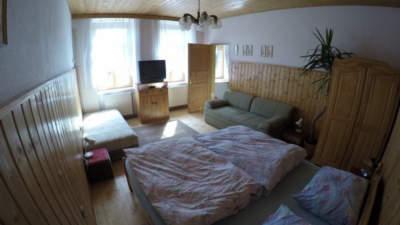 Gemütliches Schlafzimmer mit Doppelbett, Sofa, TV und Holzmöbeln in einer Ferienwohnung.