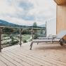 Wooden terrace with sun lounger and view of the green landscape and mountains.