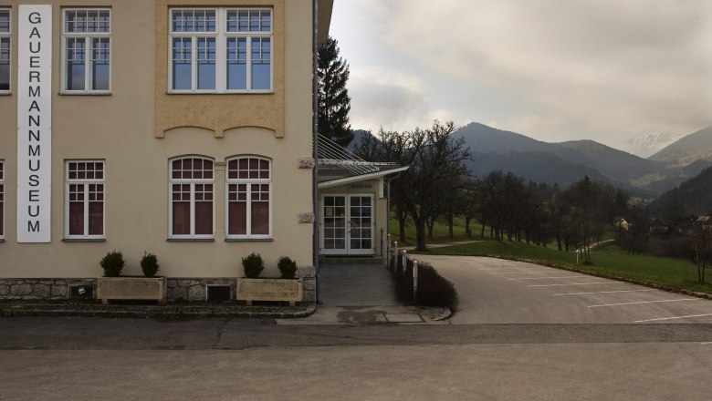 Außenansicht des Gauermannmuseums in Miesenbach mit Berglandschaft im Hintergrund.