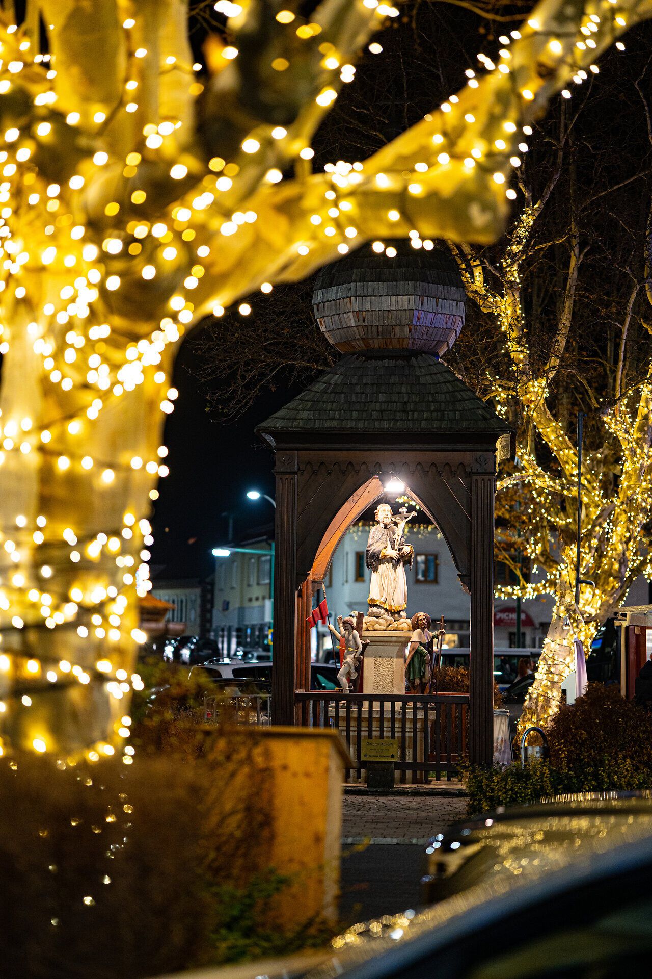 Kleine Kapelle unter einem Baum mit goldenen Lichterketten, stimmungsvoll beleuchtet bei Nacht.