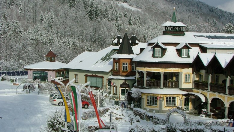 Ein verschneites Hotel im alpinen Stil mit Türmen und Balkonen, umgeben von schneebedeckten Bäumen und Hügeln.