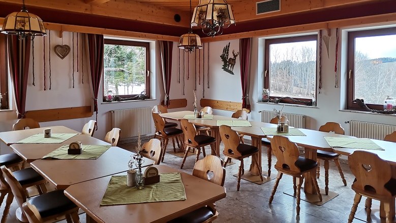 Gem&uuml;tliche Gaststube mit Holzm&ouml;beln und gr&uuml;nen Tischdecken, gro&szlig;en Fenstern und rustikaler Dekoration.