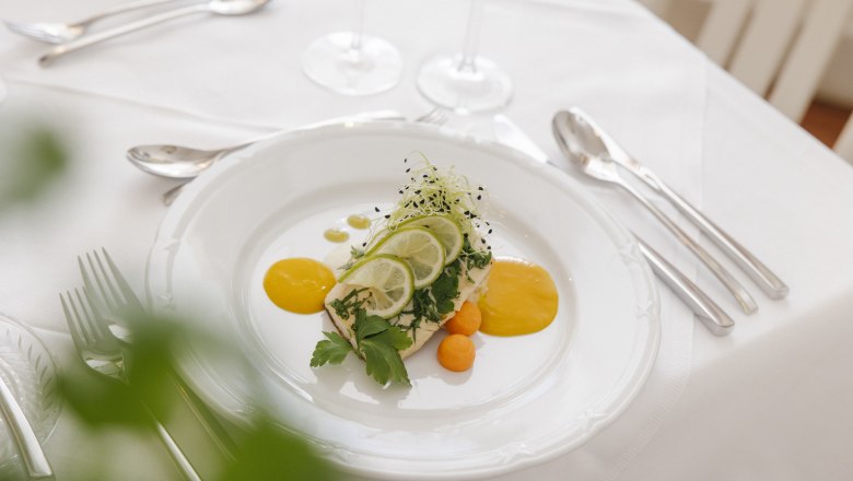 Elegant dish on a white plate garnished with lime slices and herbs on a laid table