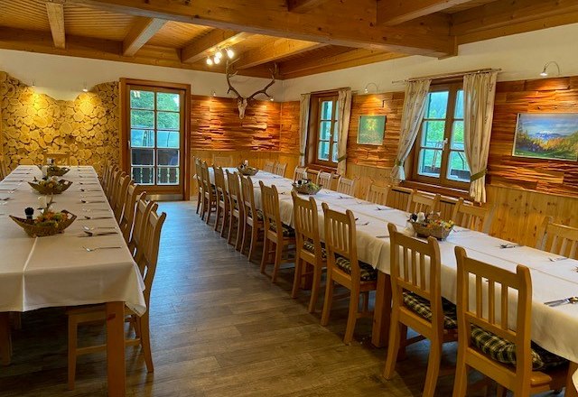 Rustikaler Speisesaal mit langen, gedeckten Tischen und Holzwänden.