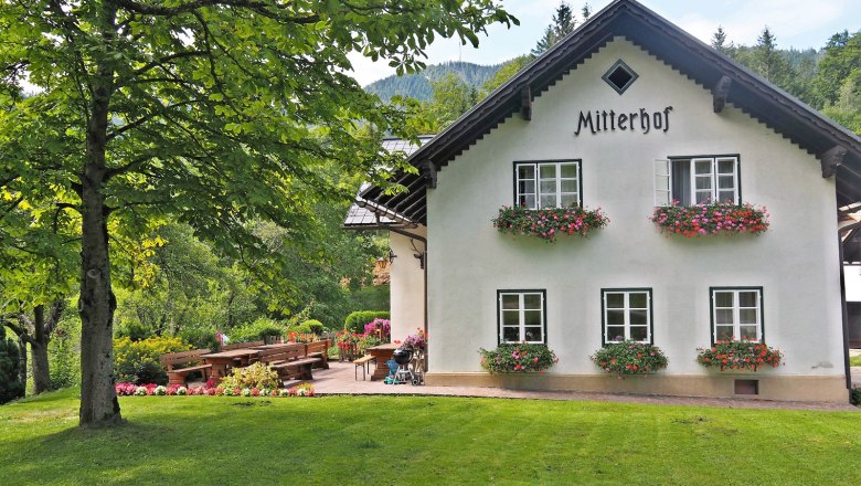 Ein traditionelles Bauernhaus mit dem Namen Mitterhof, umgeben von grüner Landschaft und Blumenbeeten.