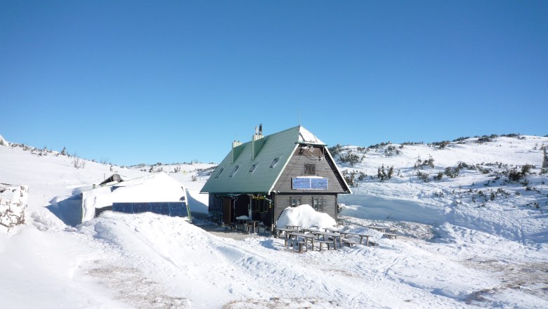 A mountain hut in the snow with solar panels and a blue sky.