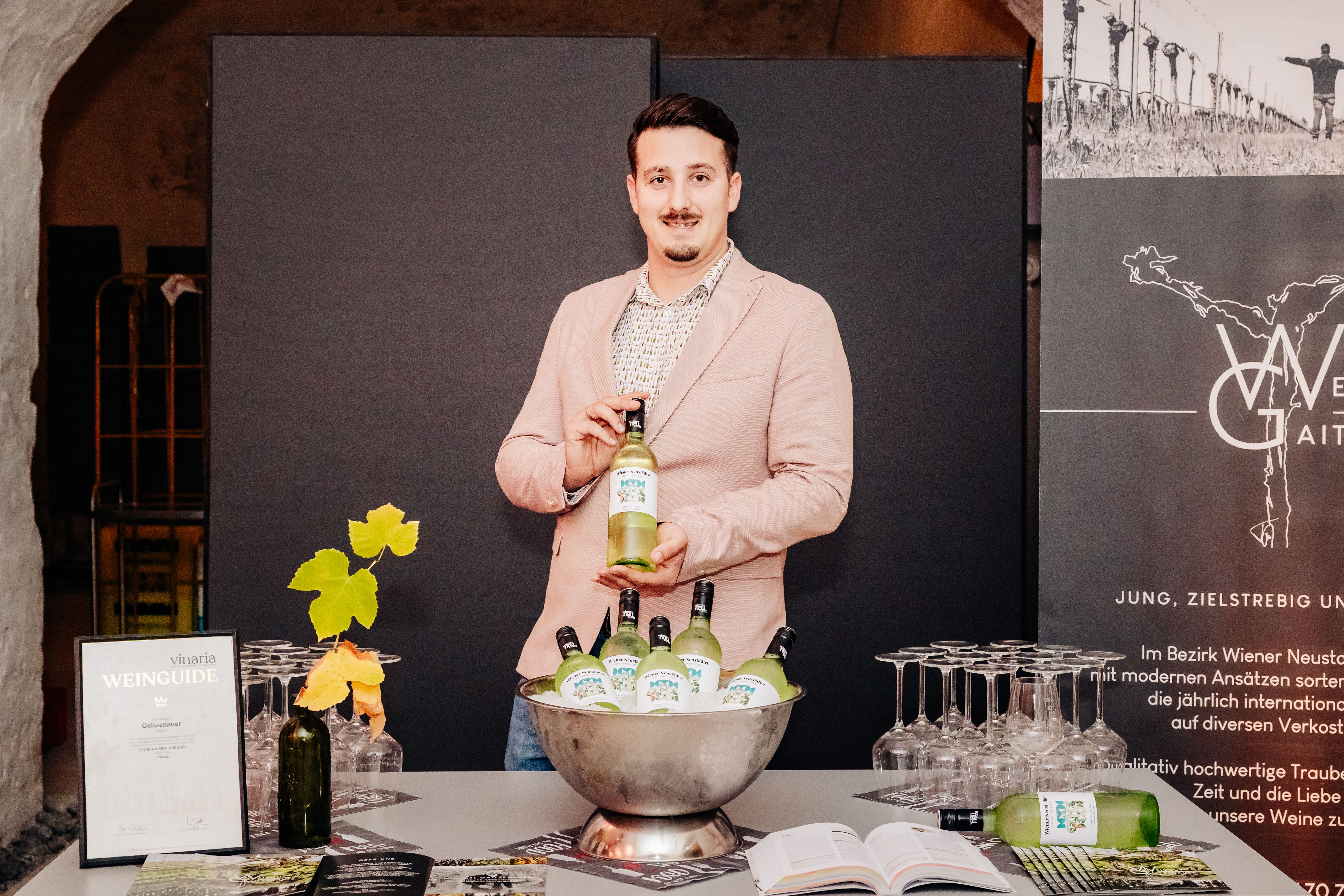 Mann präsentiert den "Wiener-Neustadt"-Wein. Er trägt ein rosa Sakko. 
