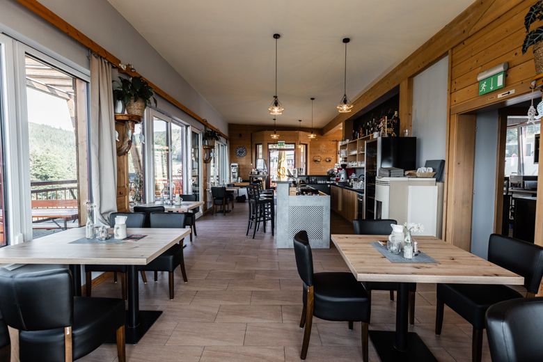 Innenansicht eines modernen Cafés mit Holzmöbeln und großen Fenstern.