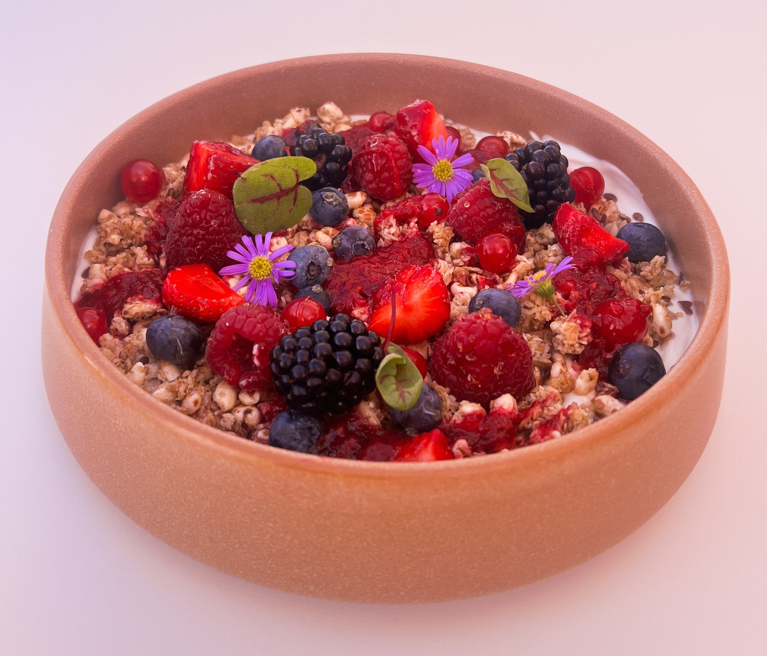 Schüssel mit Joghurt, Müsli, Beeren und essbaren Blüten.