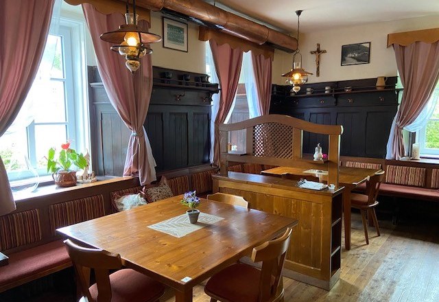 Gemütliche Gaststube mit Holzmöbeln und rosa Vorhängen.