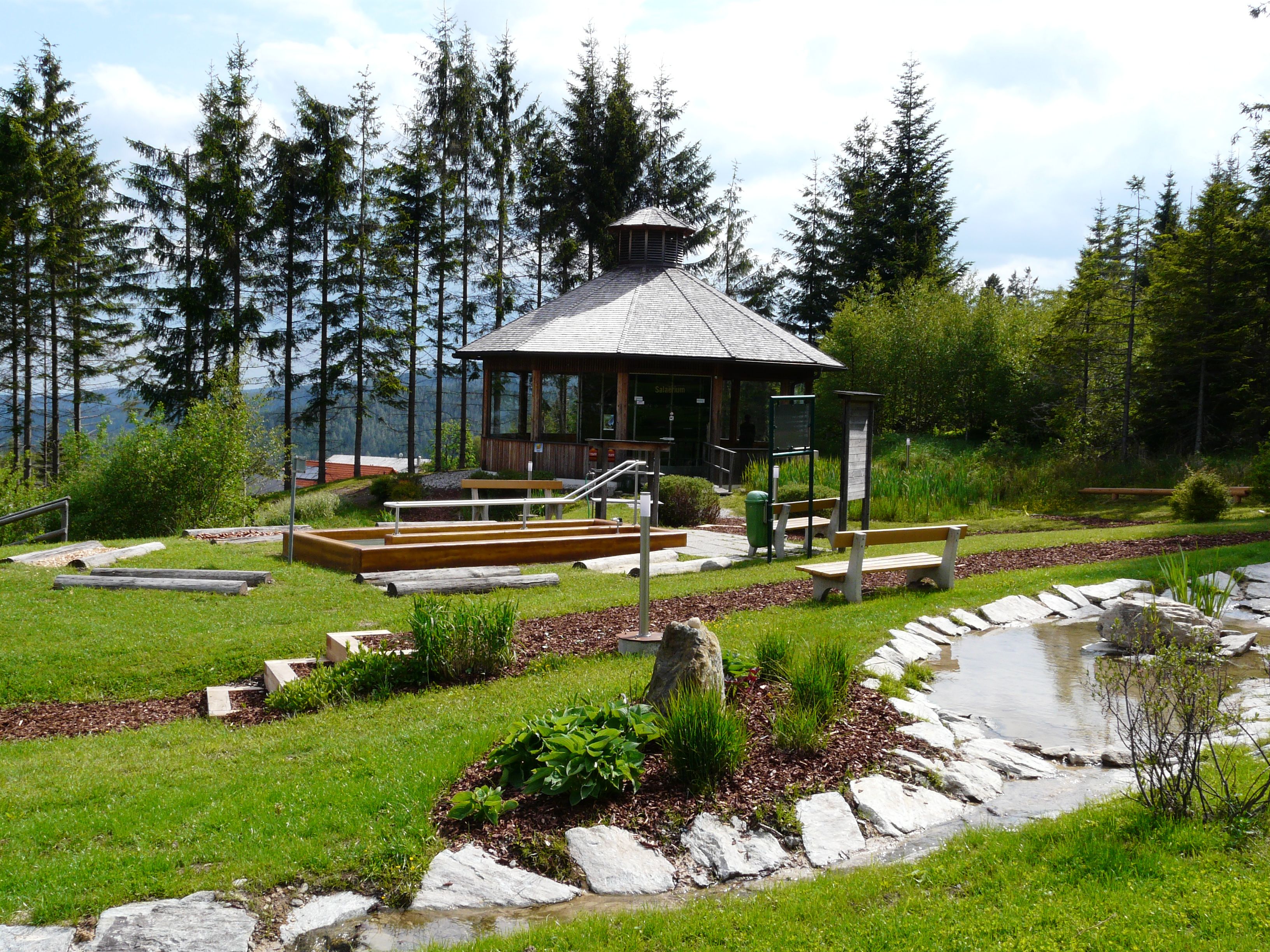 Ein kleiner Pavillon in einem grünen Park mit Bäumen und einem Teich.