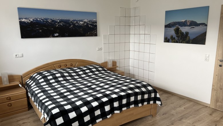 Bedroom with double bed, checkered bedspread, wooden furniture and mountain landscape pictures on the wall.