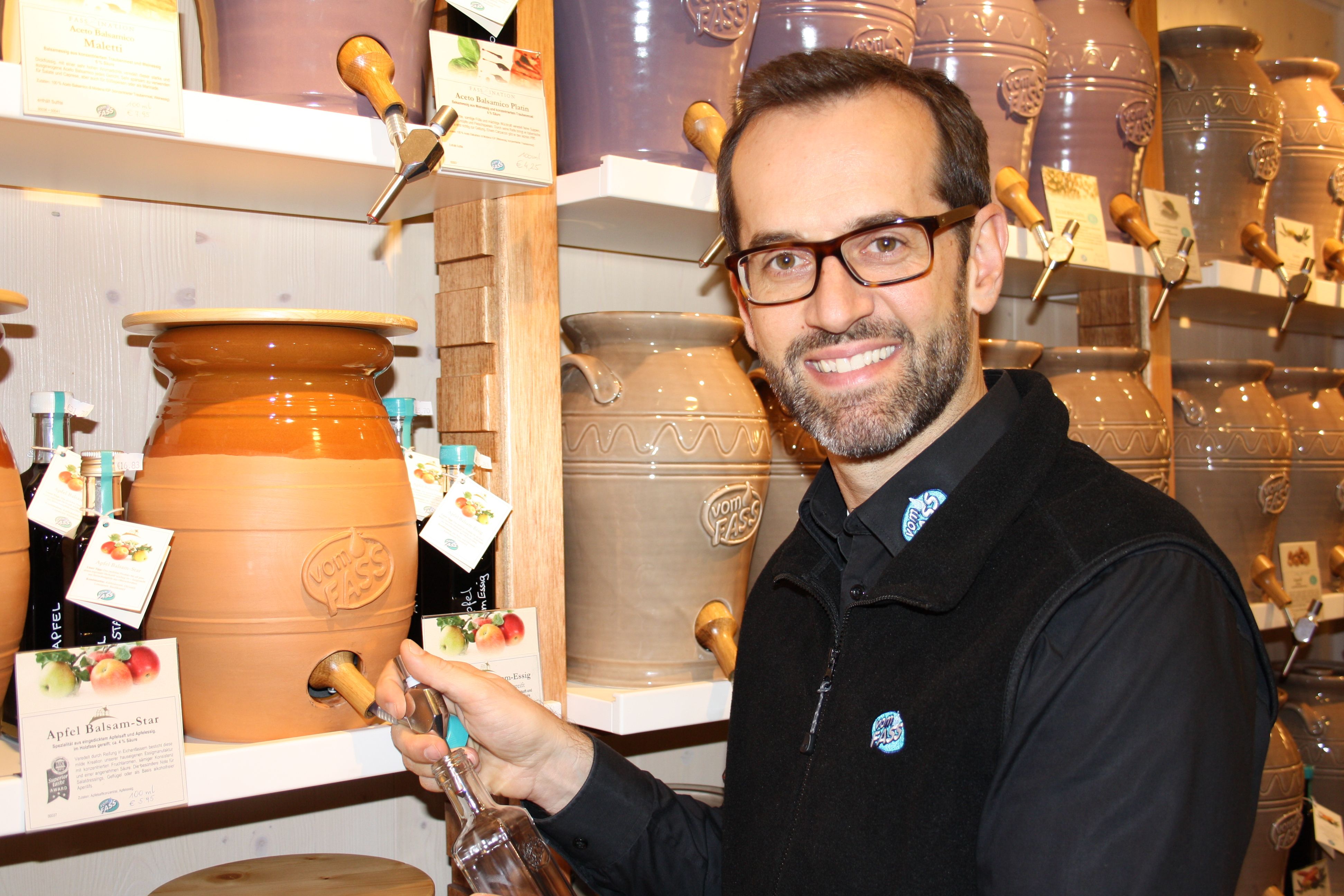 Ein Mann füllt eine Flasche aus einem großen Keramikfass bei Vom Fass.