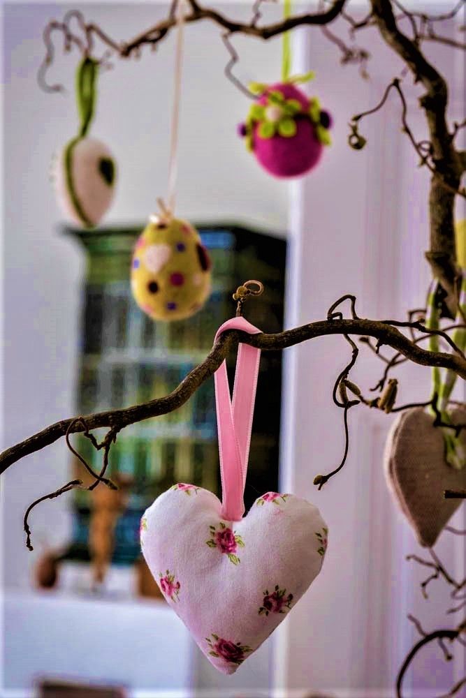 Dekorativer Ast mit hängenden Stoffherzen und bunten Eiern.