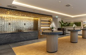 Moderner Raum f&uuml;r Seminar Kaffeepausen mit goldener Wand, schwarzen Marmortischen und Orchideen.