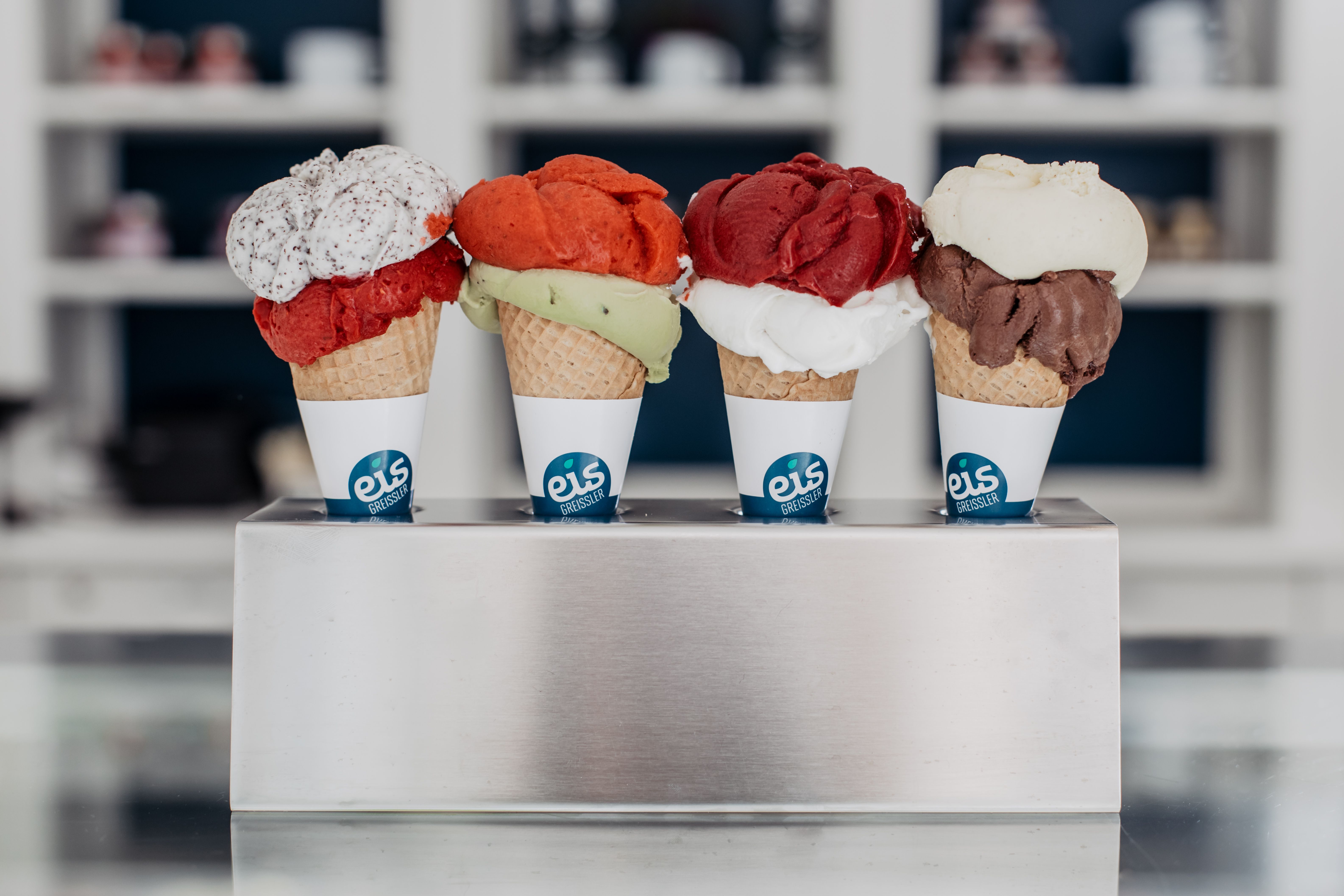 Metallhalterung mit vier Eiswaffeln, jeweils mit zwei Kugeln unterschiedlicher Eissorten.