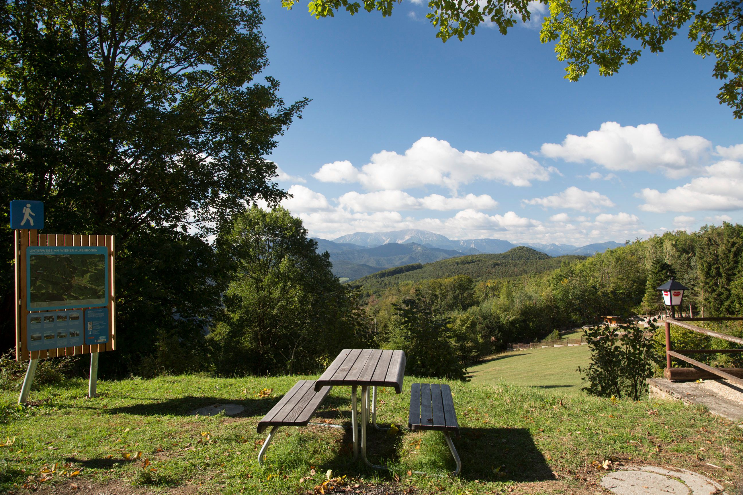 Picknicktisch mit Blick auf bewaldete Hügel und Berge, blauer Himmel mit Wolken.