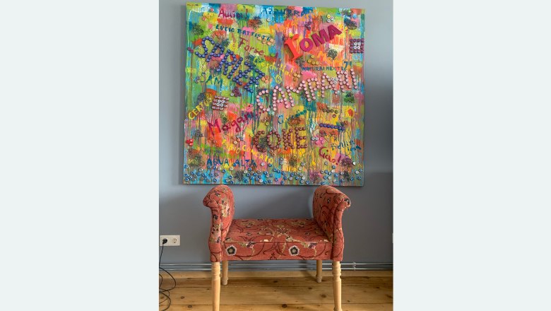 Buntes Gem&auml;lde mit Schriftz&uuml;gen &uuml;ber einer roten Bank.