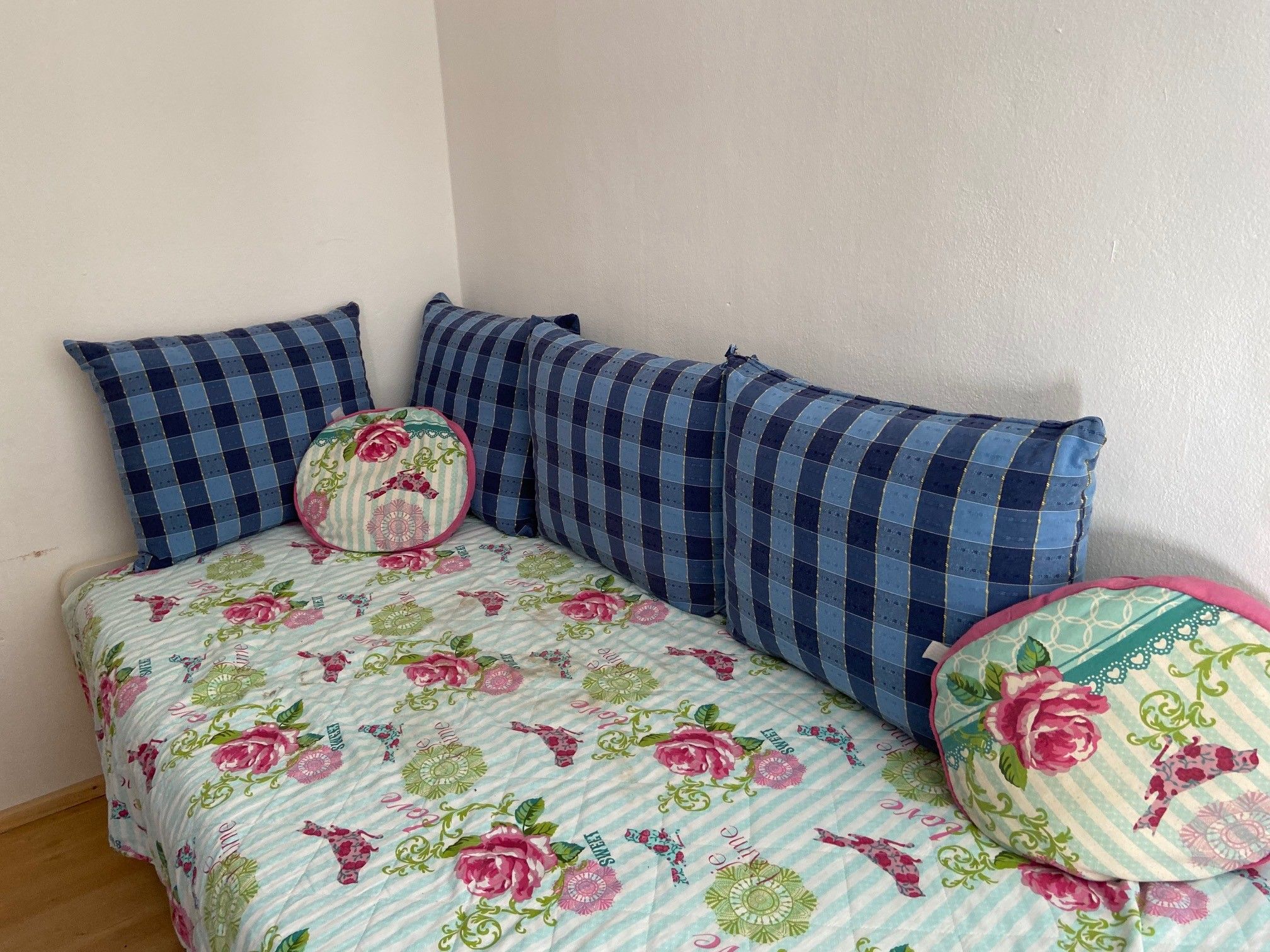 Ein Kinderzimmer mit einem Ausziehbett, das mit einer geblümten Decke und blauen Kissen dekoriert ist.