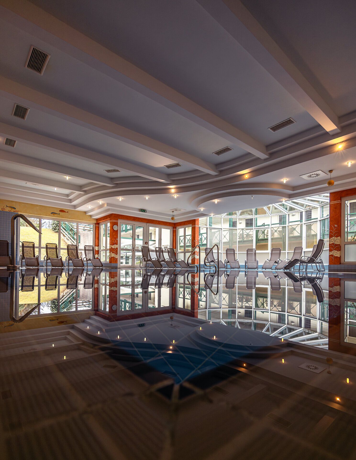 Der Innenbereich des Hotels strahlt eine einladende Atmosphäre aus, in der sich die sanften Wellen des Wassers im Pool harmonisch mit den eleganten Liegen verbinden. Große Fenster lassen das Tageslicht herein und bieten einen Blick auf die umliegende Natur, die zum Entspannen und Verweilen einlädt.