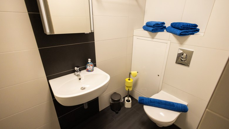 Kleines Badezimmer mit Waschbecken, Toilette, blauen Handtüchern und gelbem Toilettenpapier.
