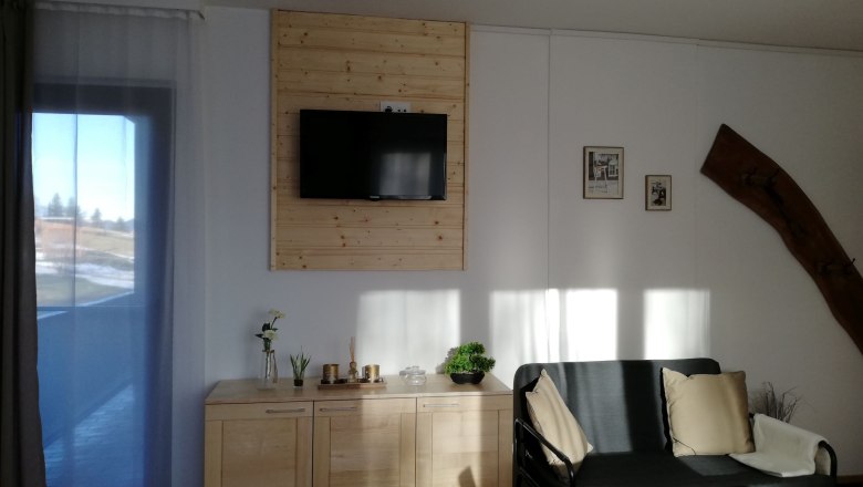 Wohnzimmer mit Sofa, Fernseher, Sideboard und Dekorationen.