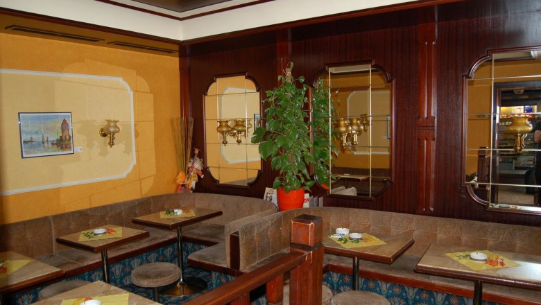 Interior view of a traditional coffee house with wooden furniture, mirrors and plants.