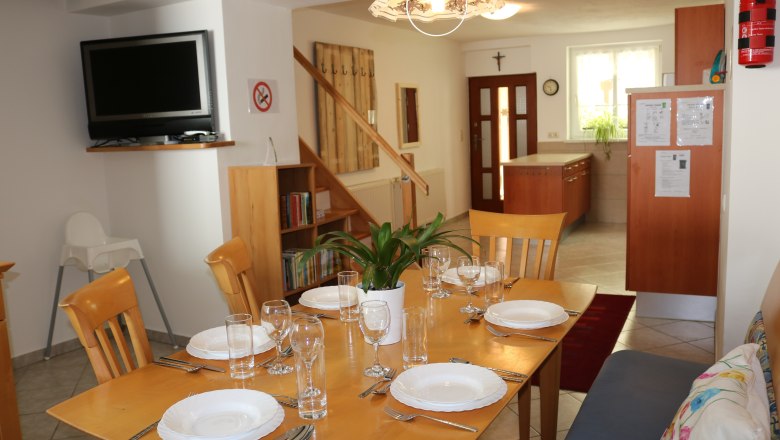 Essbereich mit gedecktem Tisch, Fernseher, Bücherregal und Küche im Hintergrund.