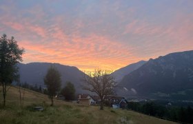 Blick auf ein Haus in einer Berglandschaft bei Sonnenuntergang.