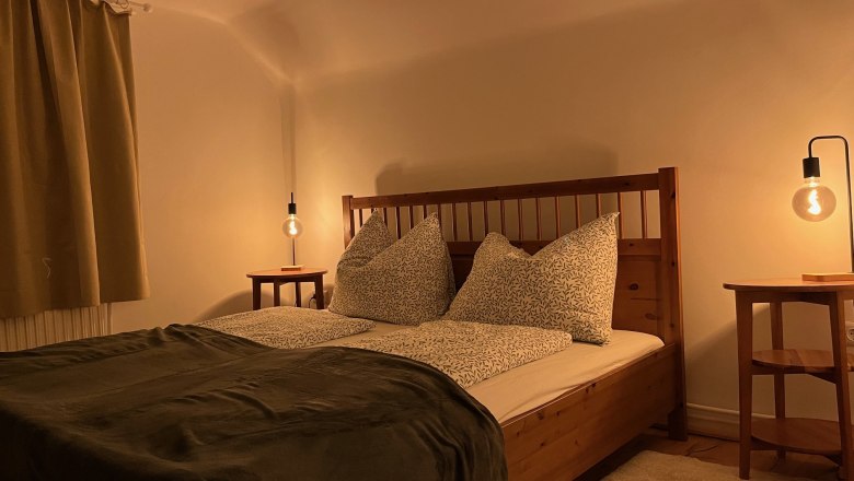 Gemütliches Schlafzimmer mit Holzbett, Nachttischen und warmem Licht.
