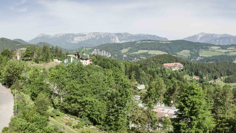Panoramablick auf eine bergige Landschaft mit Wald, Straße und Gebäuden.