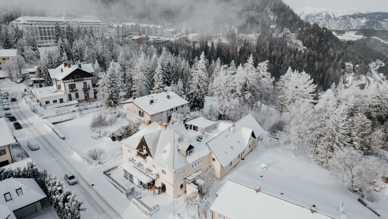 Snow-covered town with houses and trees, surrounded by mountains.