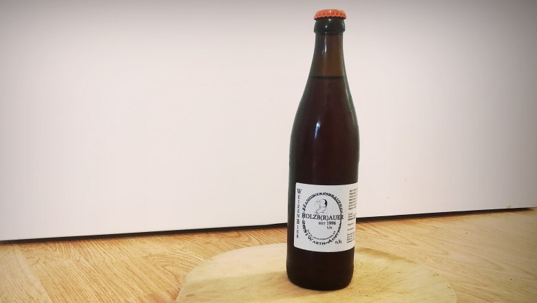 Eine Flasche Weizenbier vom Holzbräu steht auf einem runden Holzbrett mit Griff.