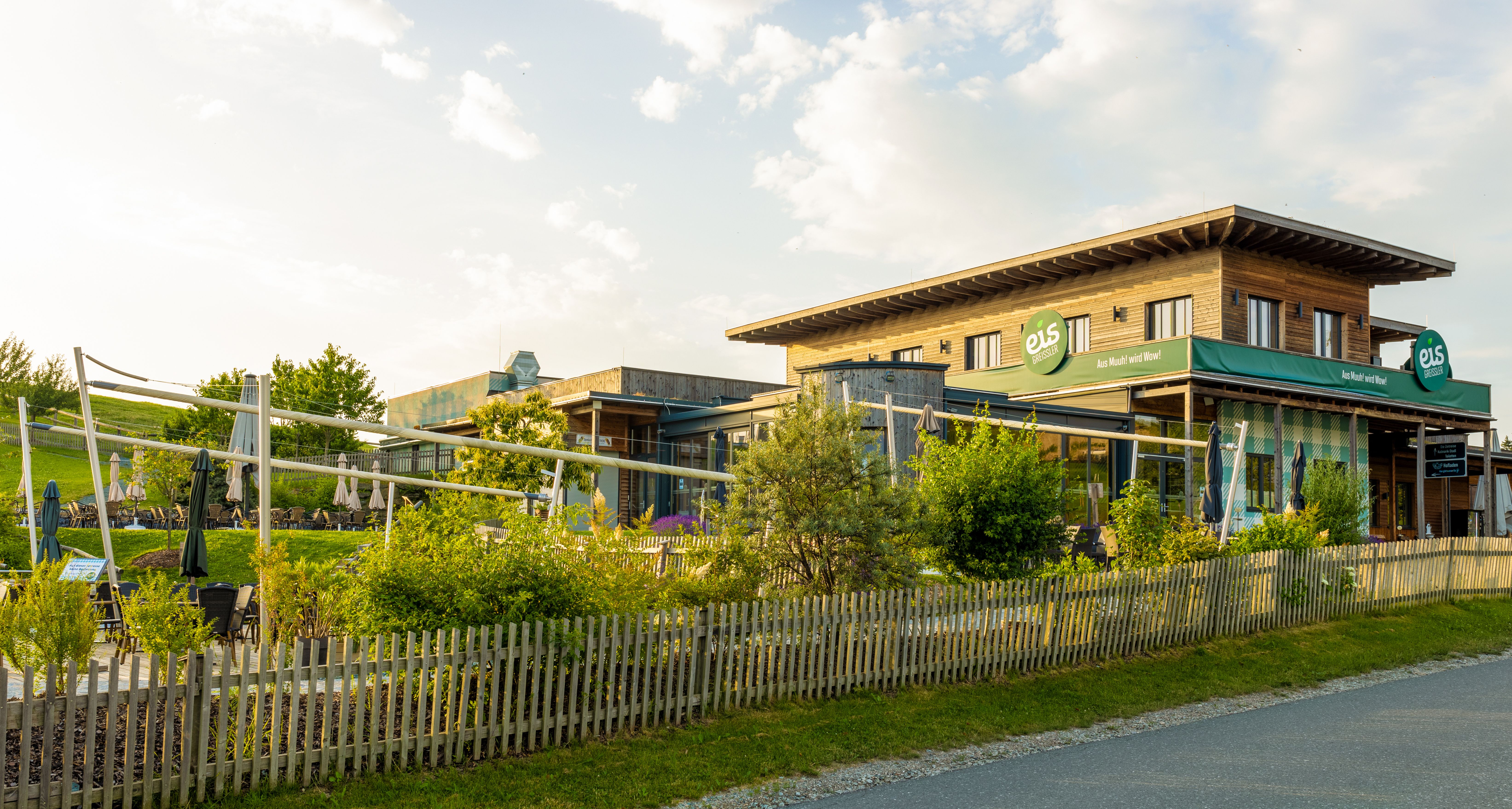 Außenansicht eines Holzgebäudes mit großer Grünfläche, Sonnenschirmen und einem Holzzaun.