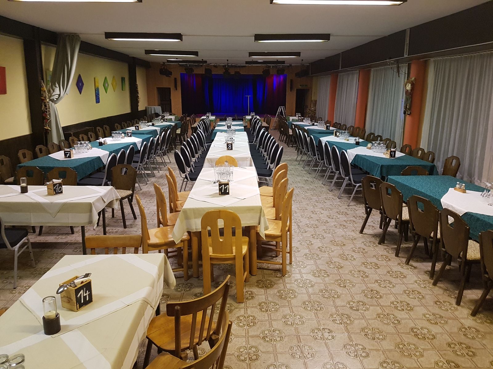 Ein leerer Veranstaltungssaal mit gedeckten Tischen und einer Bühne im Hintergrund.