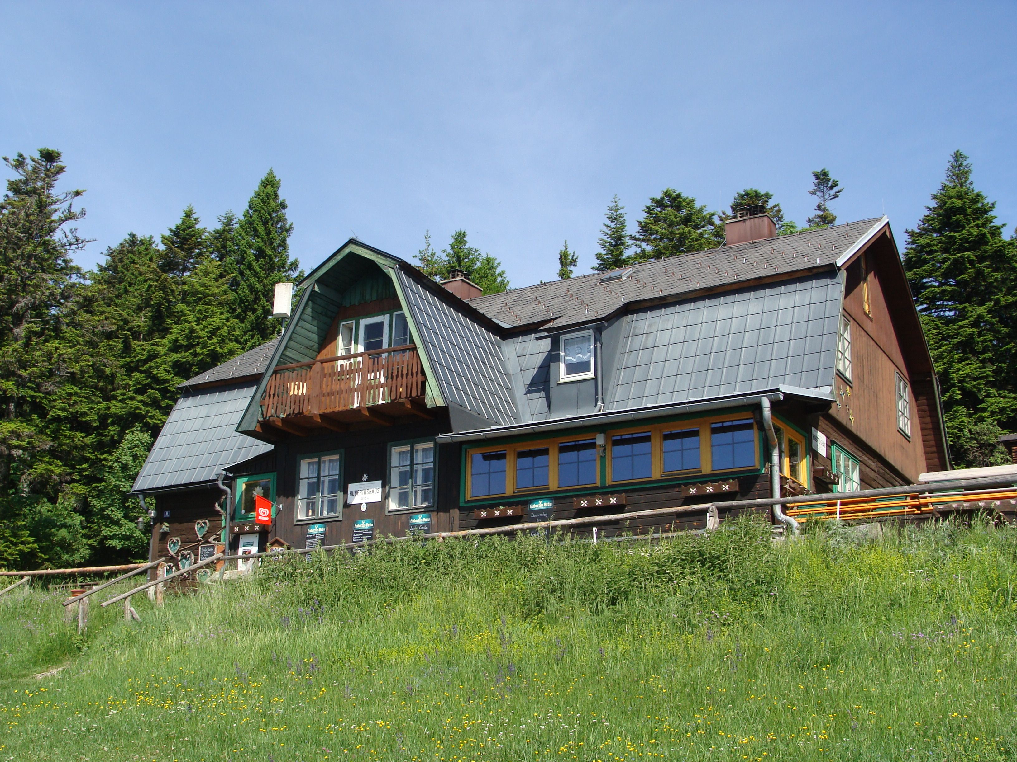 Ein traditionelles Berghaus mit Holzfassade und Schindeldach, umgeben von Bäumen und Wiese.