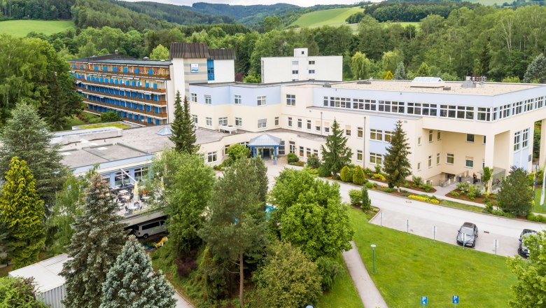 Vor einem Park ein hellgelbes Geb&auml;ude mit Flachdach