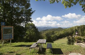 Picknicktisch mit Blick auf bewaldete Hügel und Berge, blauer Himmel mit Wolken.