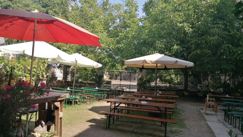 Ein ruhiger Innenhof mit Holzbänken und Tischen unter großen Sonnenschirmen und Bäumen.