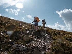 Die Wanderer erklimmen den sanften Hang, umgeben von üppigem Grün und dem strahlenden Licht der Sonne. Die frische Bergluft und die atemberaubenden Ausblicke laden dazu ein, die Schönheit der Natur in vollen Zügen zu genießen.