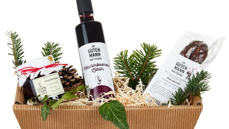Geschenkkorb mit Likör, Marmelade und Wurst, dekoriert mit Tannenzweigen.