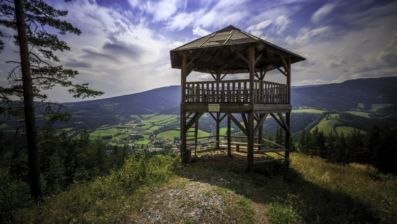 Holzaussichtsturm mit Blick auf grüne Täler und Berge unter blauem Himmel.