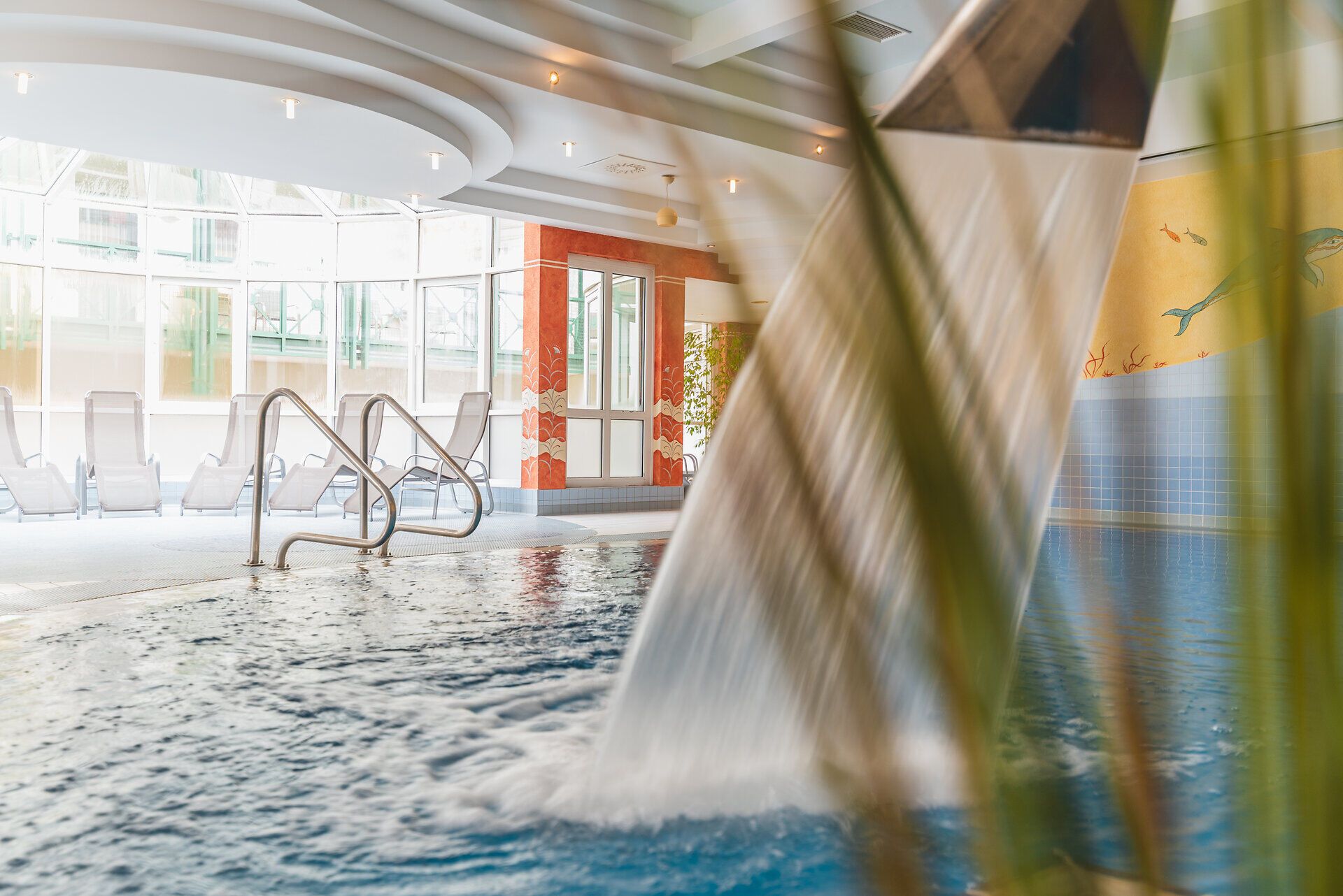 Tauchen Sie ein in die entspannende Atmosphäre des Innenpools, wo sanfte Wasserfälle und helles Licht eine Oase der Ruhe schaffen. Umgeben von modernen Liegen und einem Hauch von Natur, ist dieser Ort ideal, um nach einem Tag in den Wiener Alpen zu entspannen.