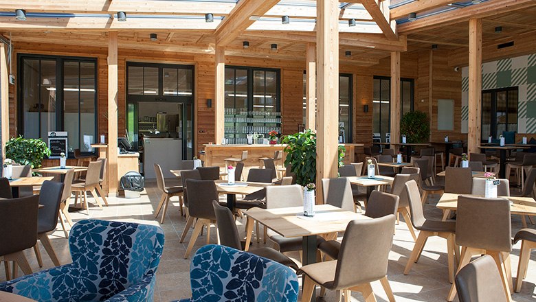 Ein modernes Kaffeehaus mit vielen Holzelementen, eckigen Tischen und braunen und blauen Stühlen.