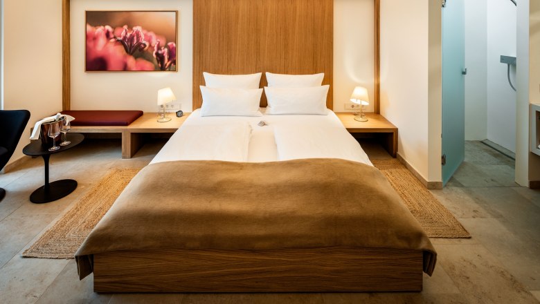 Modern eingerichtetes Hotelzimmer mit Doppelbett, Nachttischen, Lampen und einem Bild an der Wand.