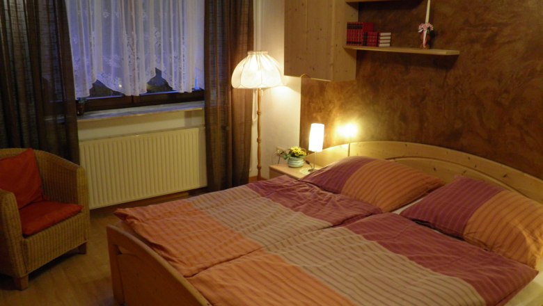 Gemütliches Schlafzimmer mit Doppelbett, Nachttischlampen, Bücherregal und Sessel.