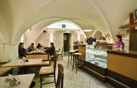 Interior view of a cozy caf&eacute; with a vaulted ceiling, tables and a bar.