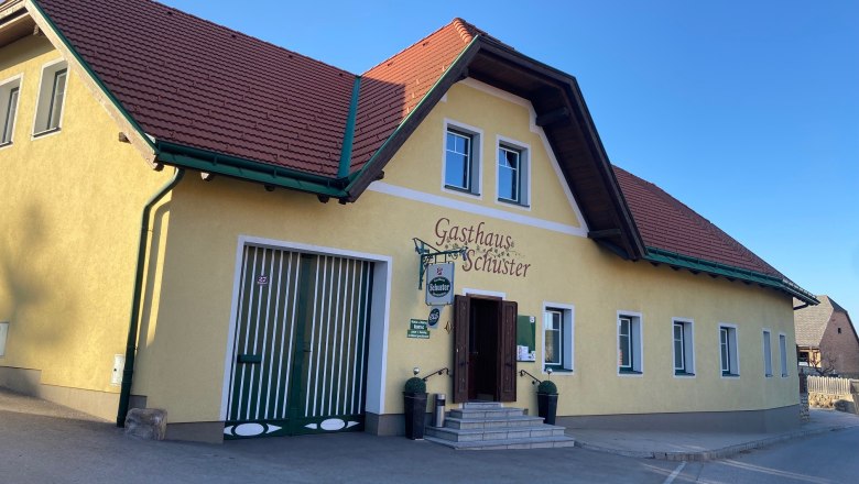 Gelbes Geb&auml;ude mit rotem Dach, beschriftet als Gasthaus Schuster.